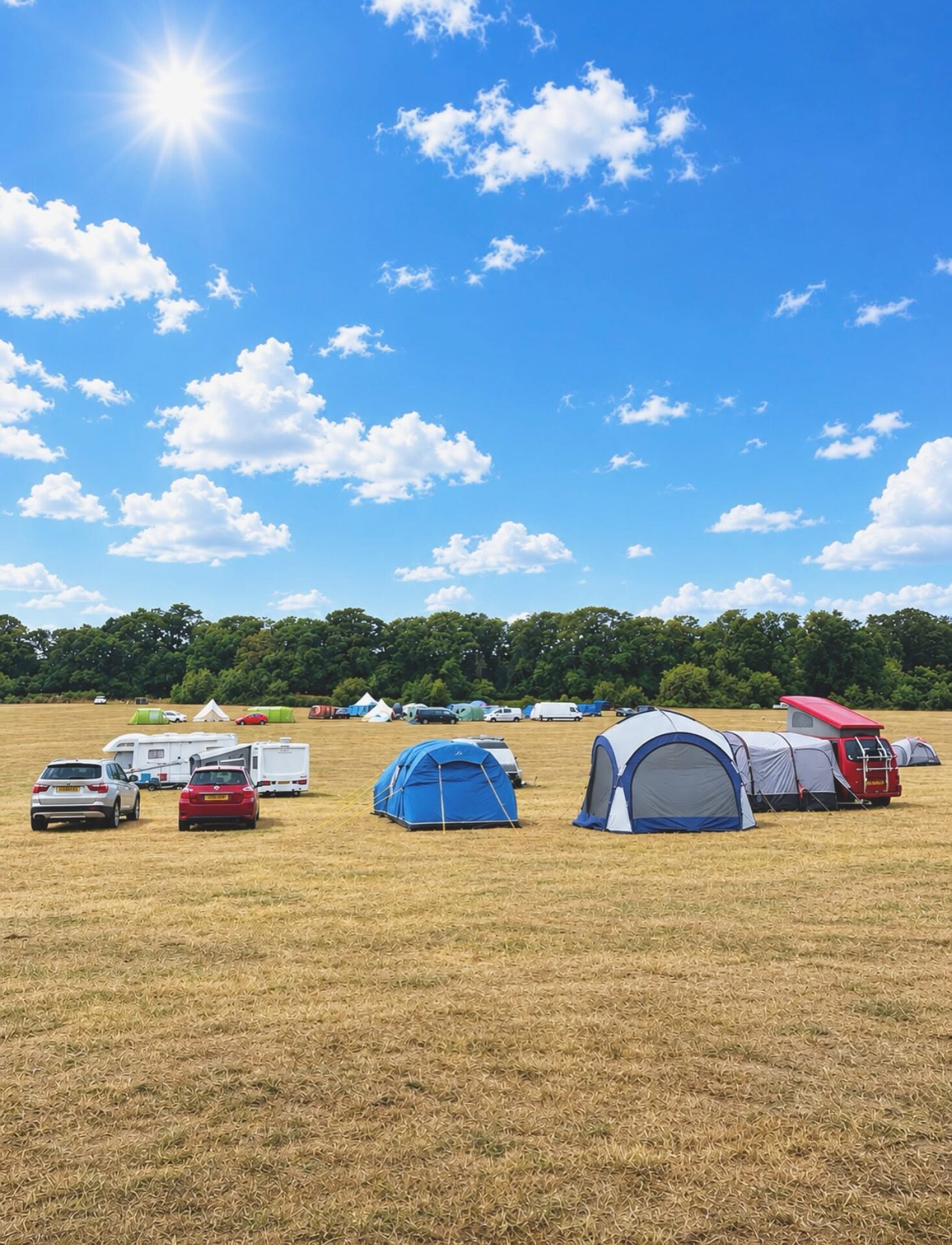 Tents and campers in a sunny field beneath clouds